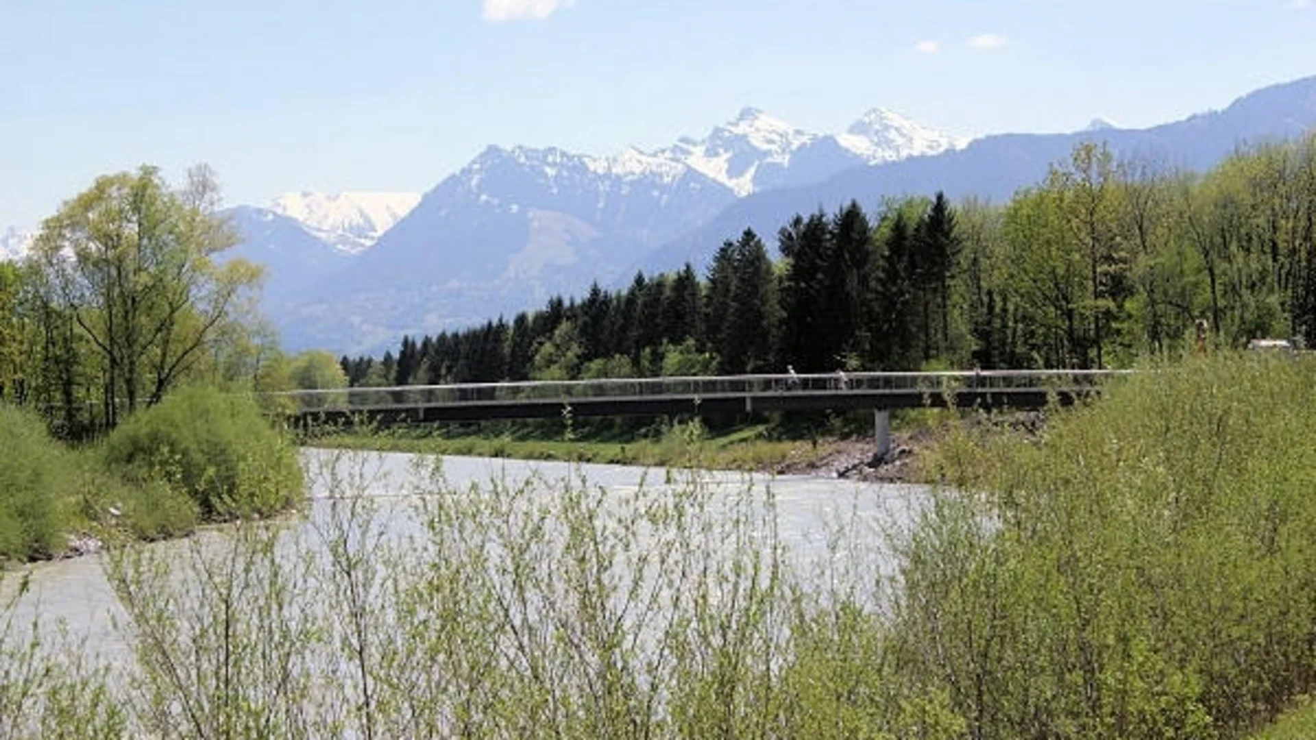 Fluss mit Brücke und schneebedeckten Bergen im Hintergrund