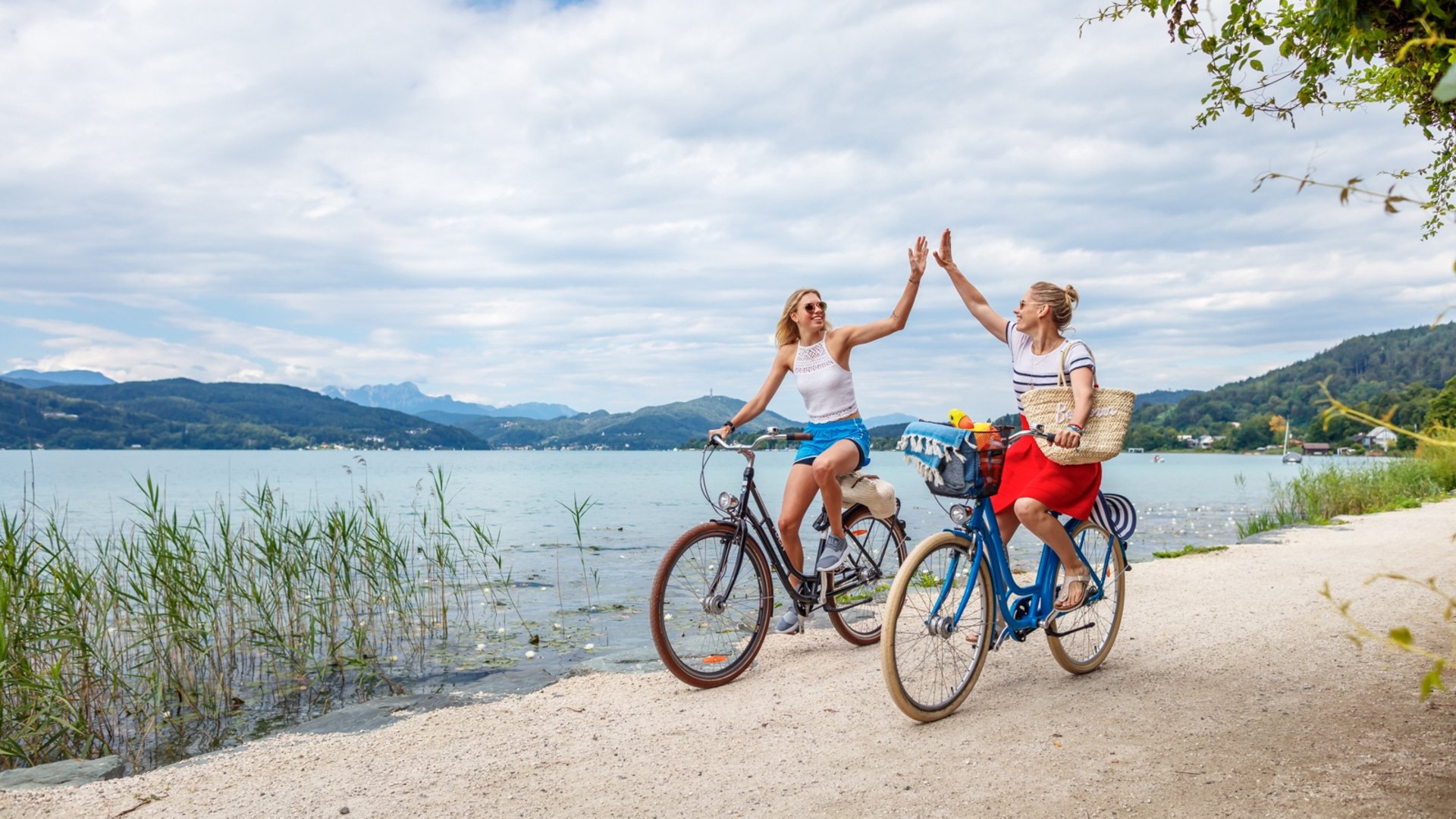 Two women on bikes high five by the lakeside path