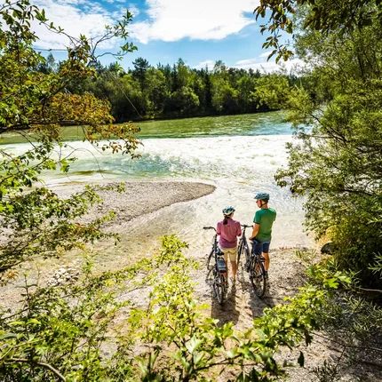 Twee fietsers bij rivieroevers tussen bomen kijken naar het water