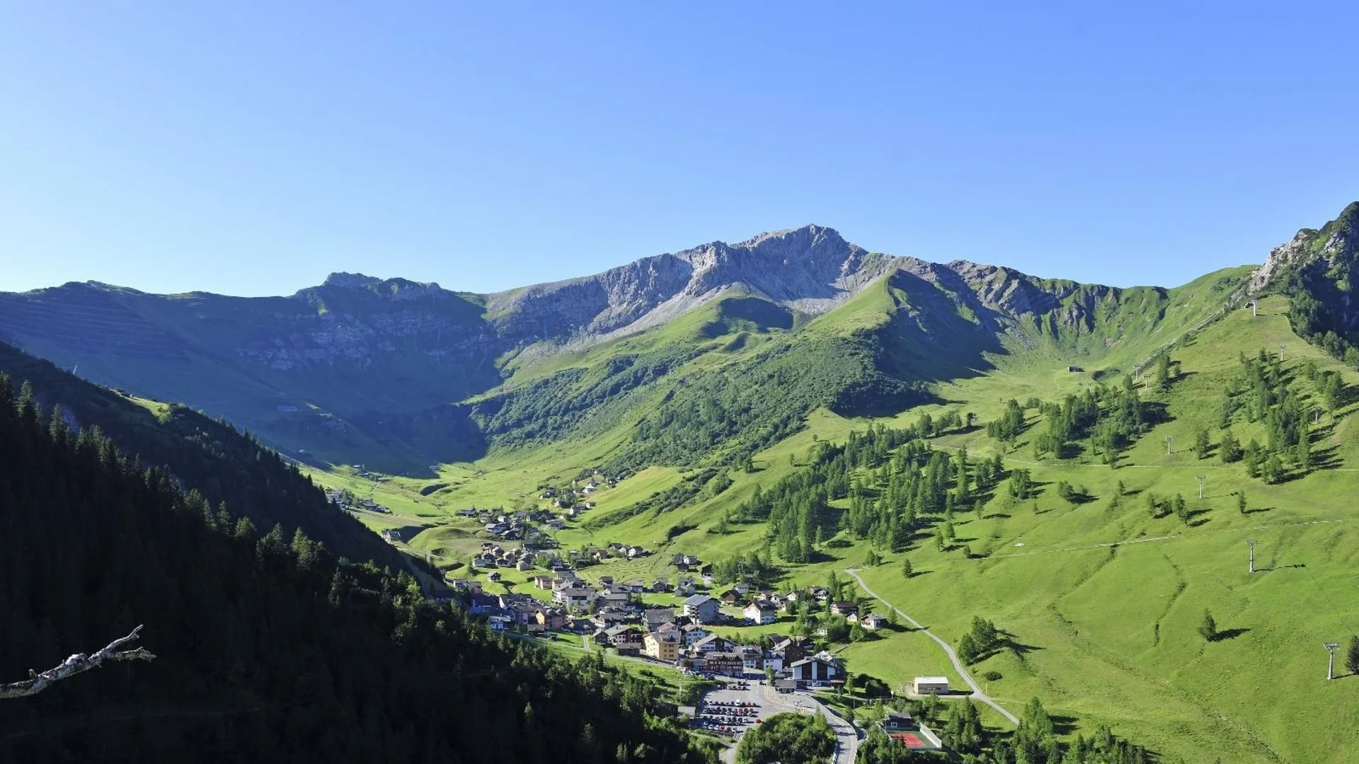 Dorf in grünem Tal umgeben von Bergen unter klarem blauem Himmel