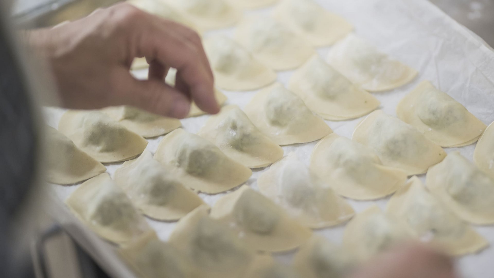 Hand placing fresh ravioli on baking sheet with parchment paper