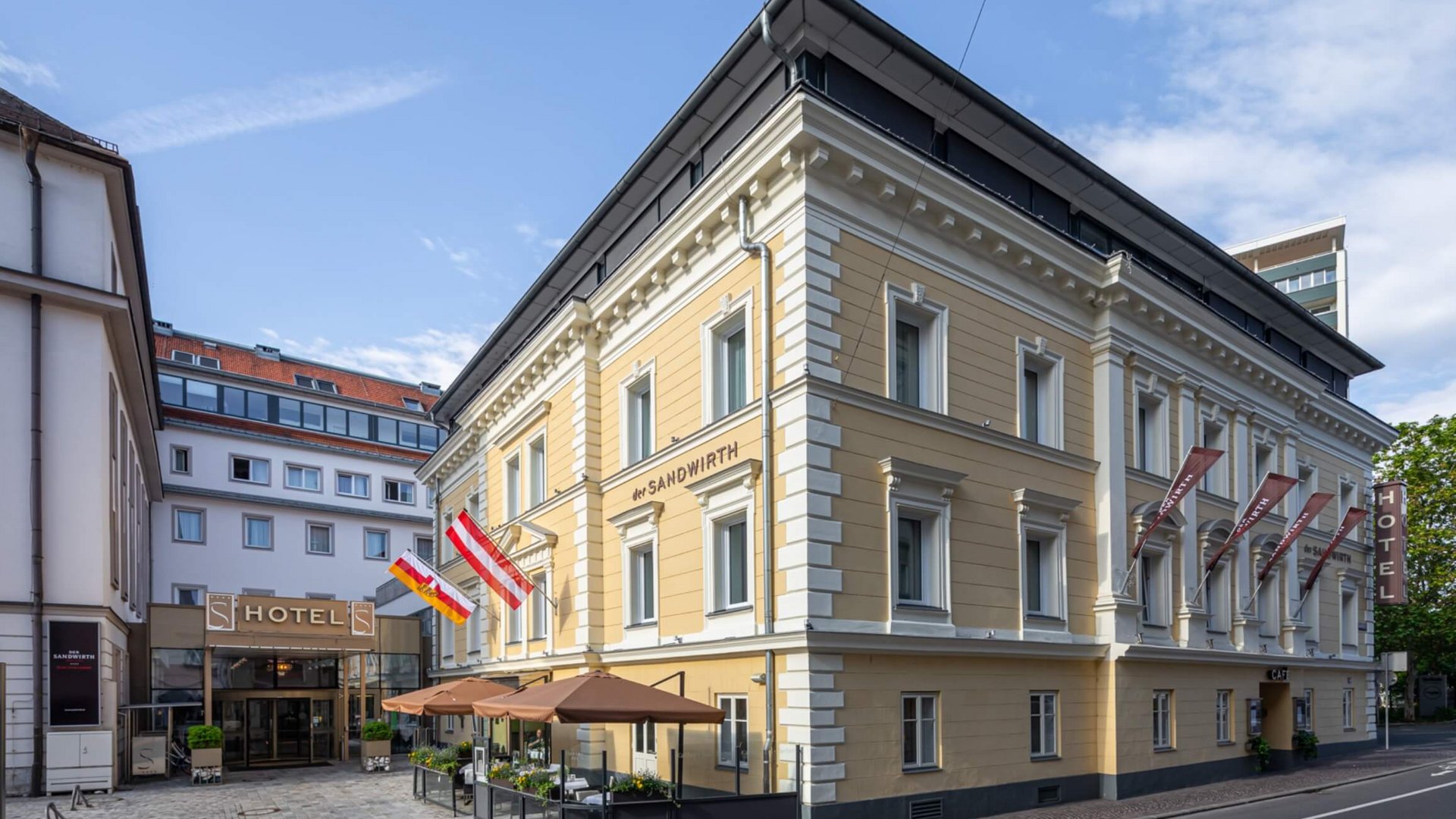 Yellow hotel building with flags and outdoor seating on a sunny day