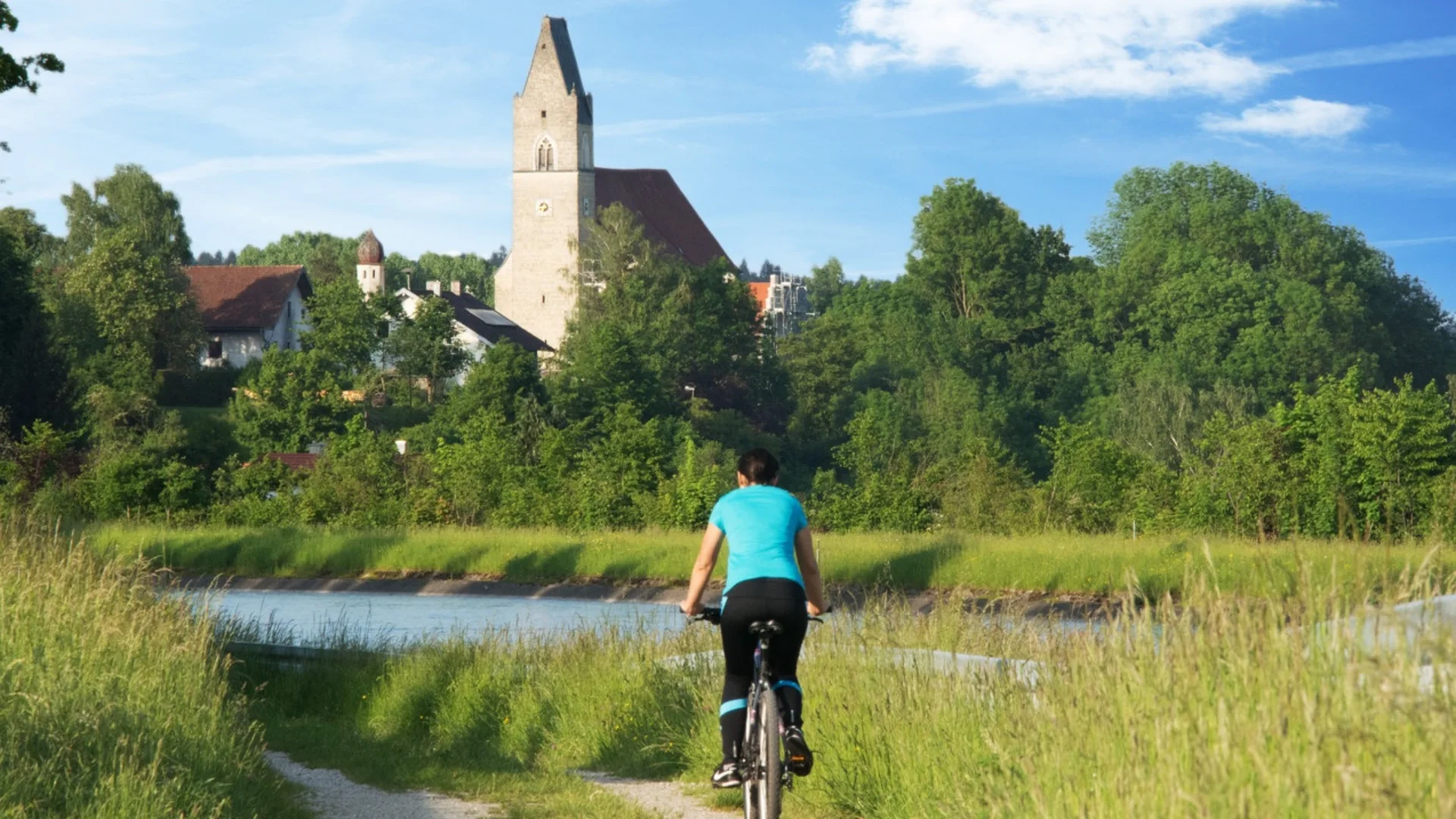 Fahrradfahrerin auf einem Weg mit Kirche und Bäumen im Hintergrund