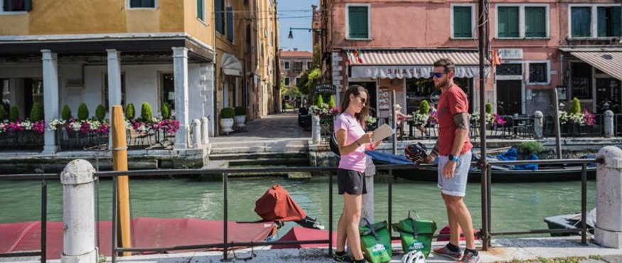Two cyclists standing by a canal in a city with colorful buildings