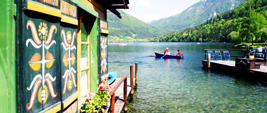View of a lake with boathouse, rowboat, and mountains in the background