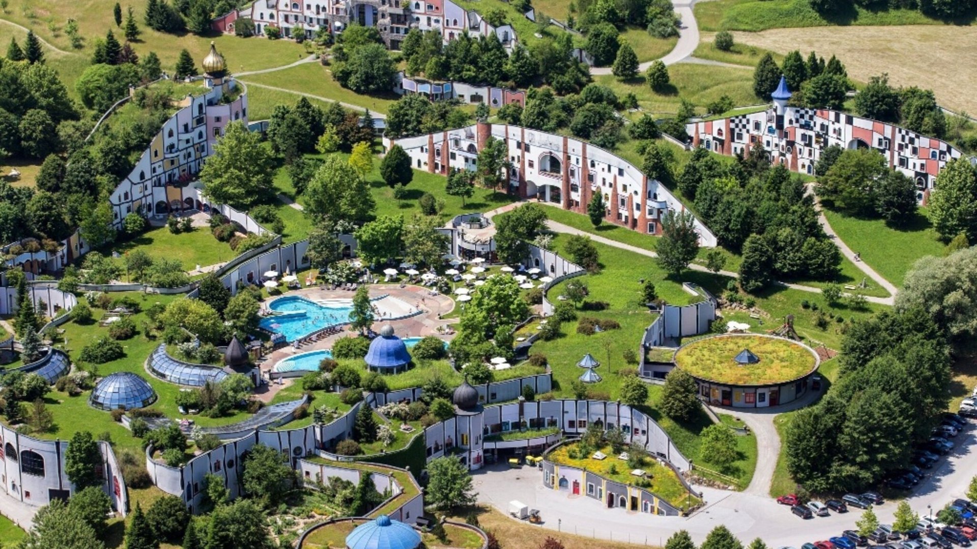 Aerial view of green architectural complex with curvy buildings and a pool