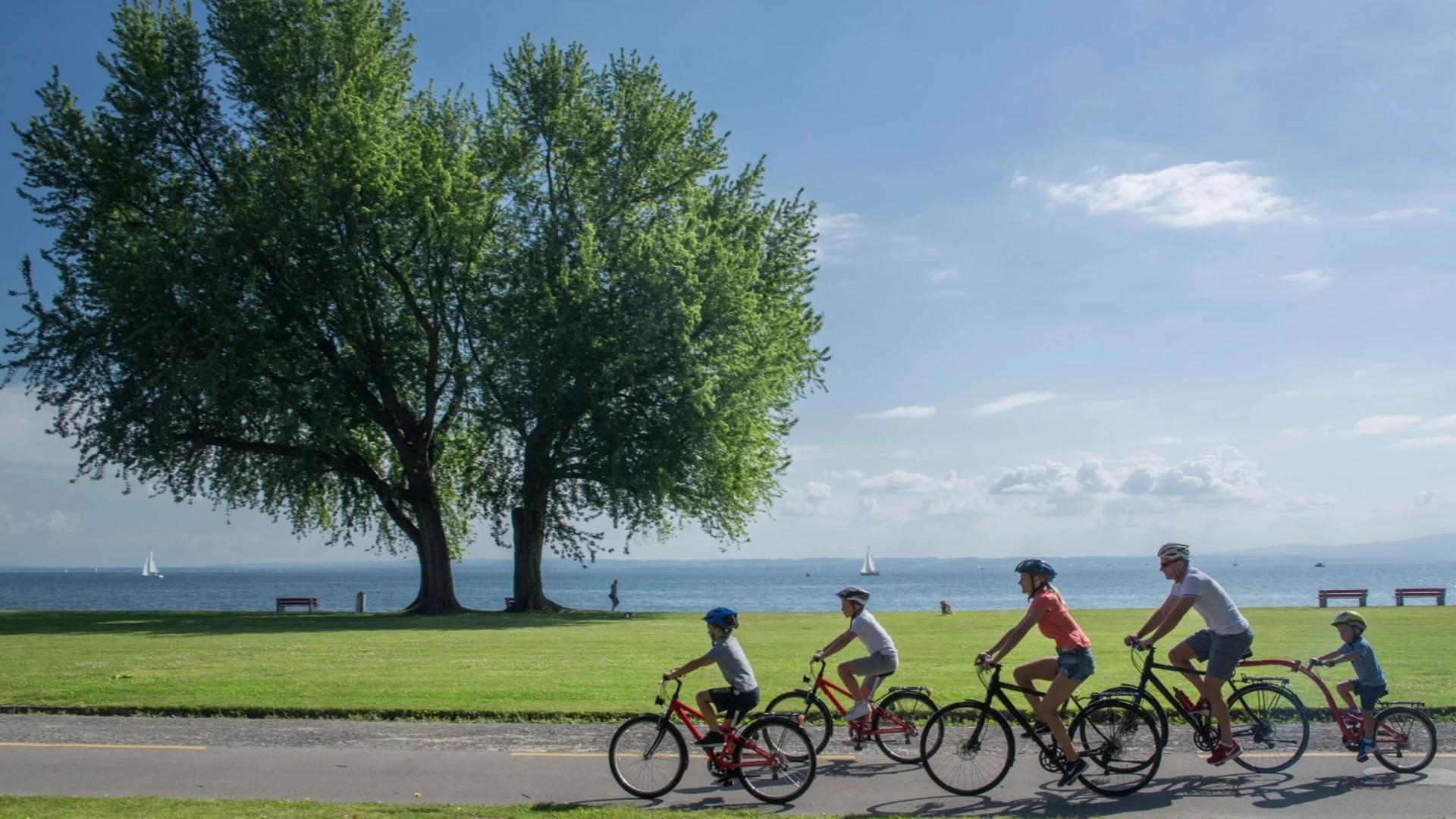 Family with three kids cycling on a lakeside path on a sunny day