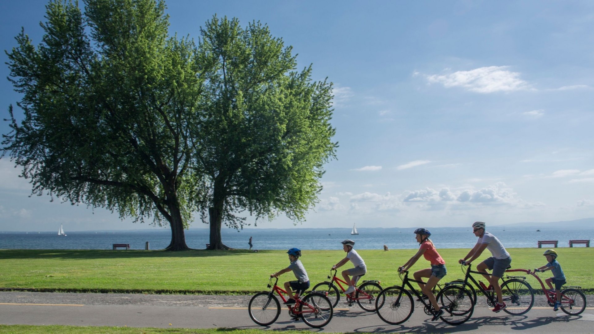 Family with three kids cycling on a lakeside path on a sunny day