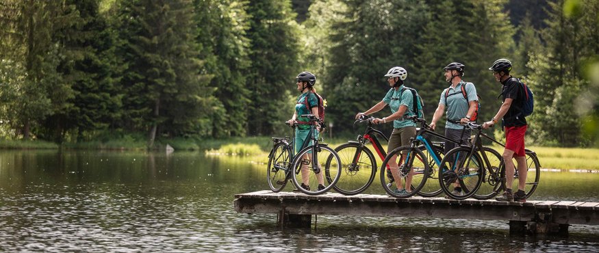 Four cyclists with helmets standing with bikes on a pier by a lake