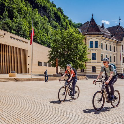 Zwei Radfahrer vor historischen Gebäuden in sonnigem Stadtplatz