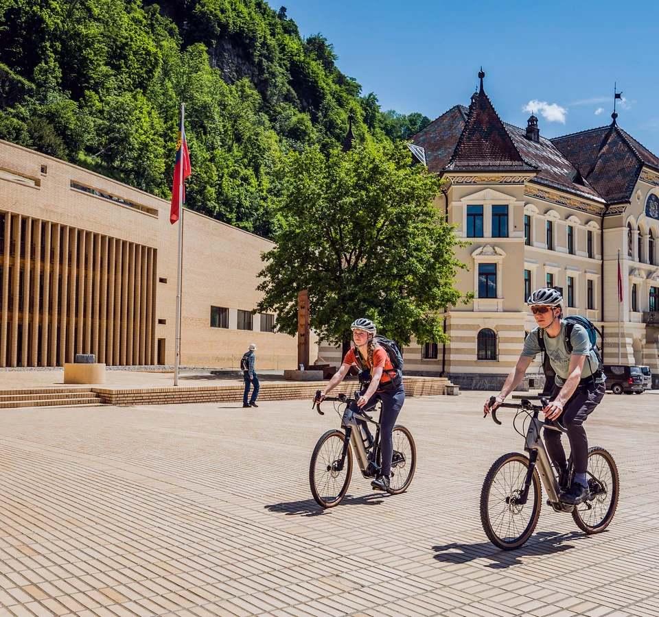 Zwei Radfahrer vor historischen Gebäuden in sonnigem Stadtplatz