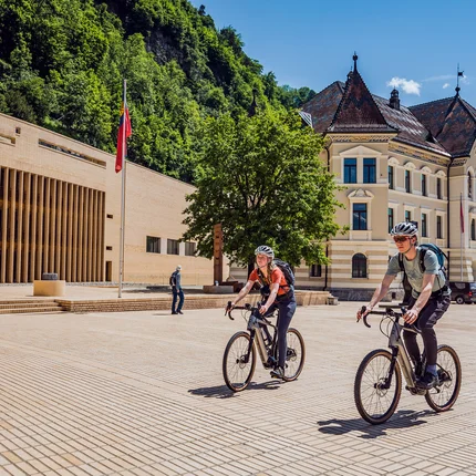 Zwei Radfahrer vor historischen Gebäuden in sonnigem Stadtplatz