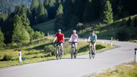 Drei Radfahrer fahren auf einer Landstraße durch grüne Berge