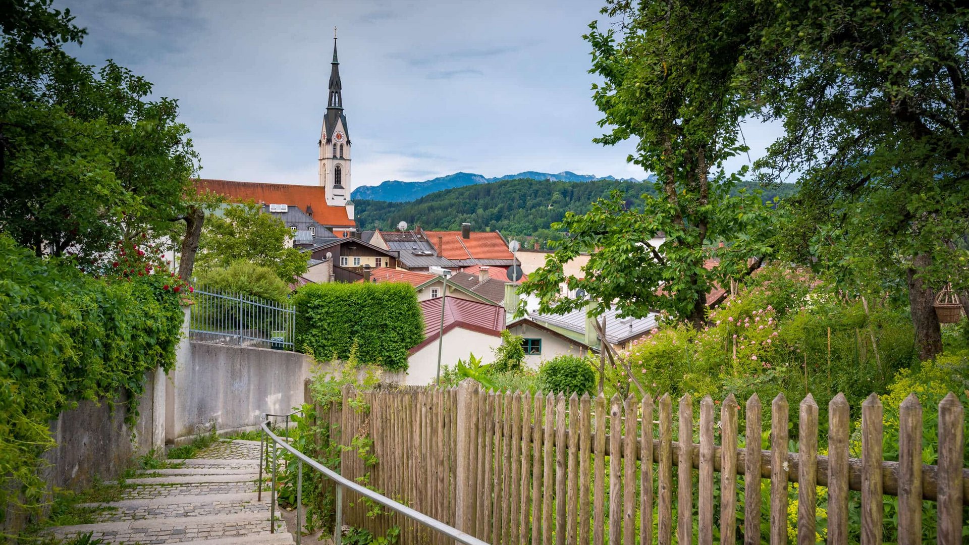 Narrow stairway path with wooden fence and church steeple in a green village