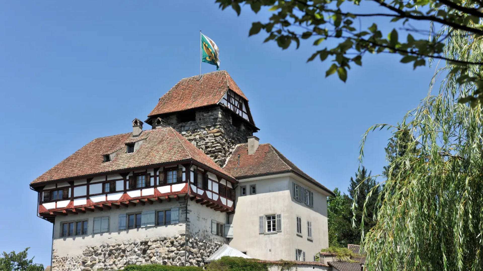 Historic castle with red tiled roof and flag under clear blue sky