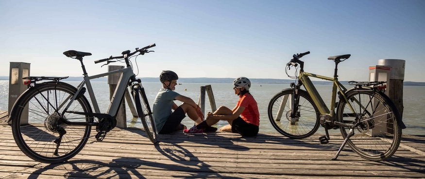 Two cyclists sitting on a dock by the lake with their bikes beside them