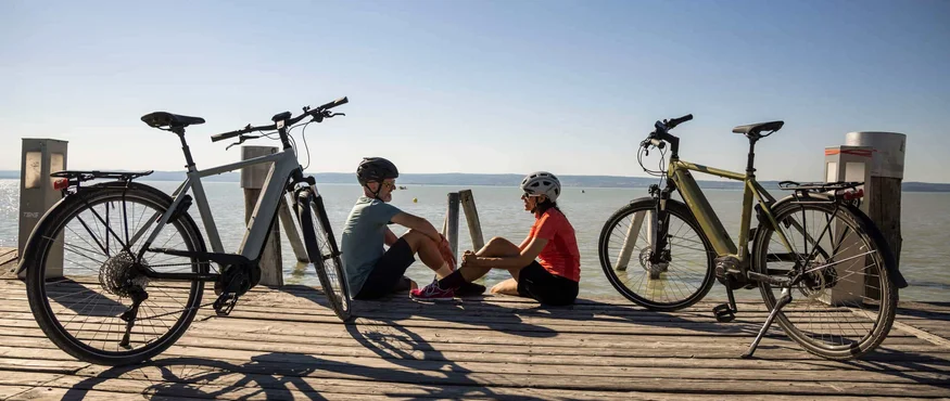 Zwei Radfahrer sitzen auf einem Steg am See mit ihren Fahrrädern daneben
