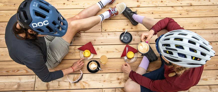 Twee fietsers met helmen drinken koffie en eten taart op houten terras