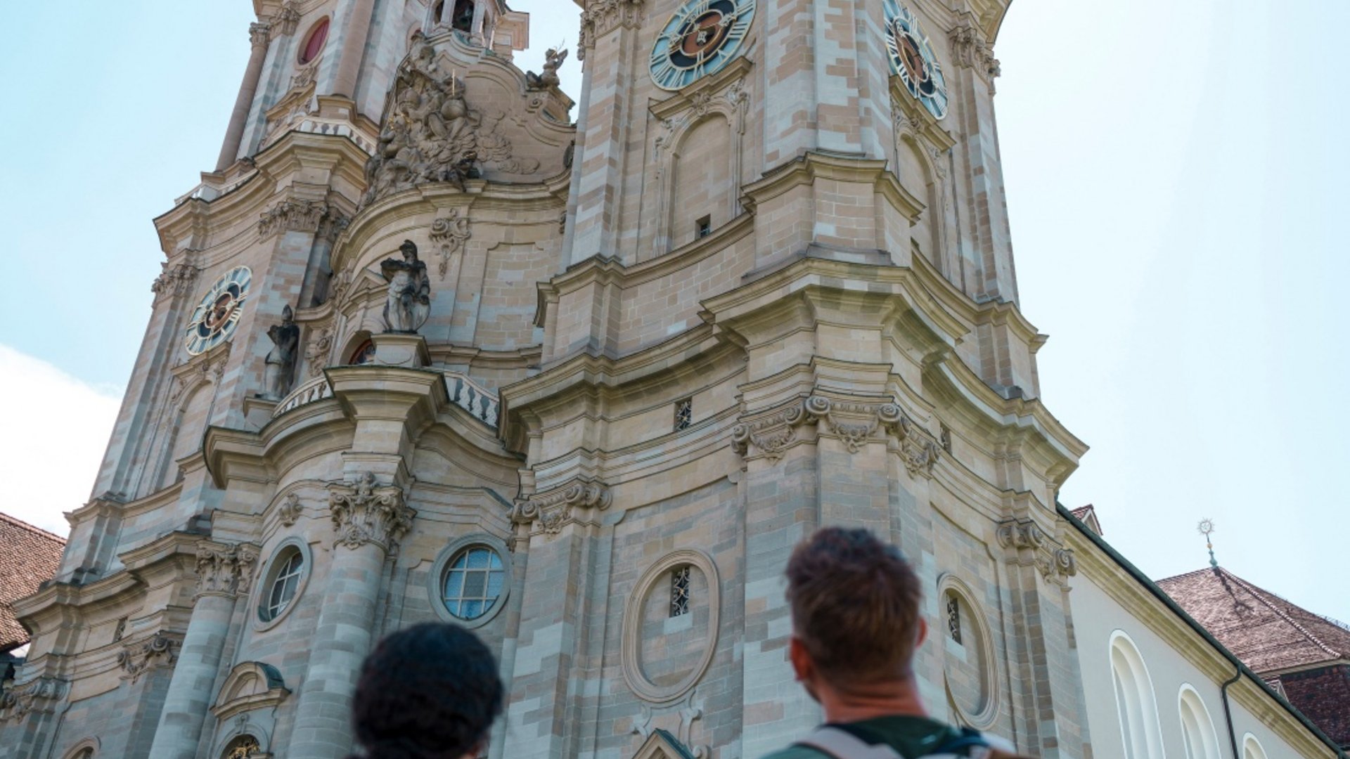 Two people with backpacks looking up at a baroque church tower facade