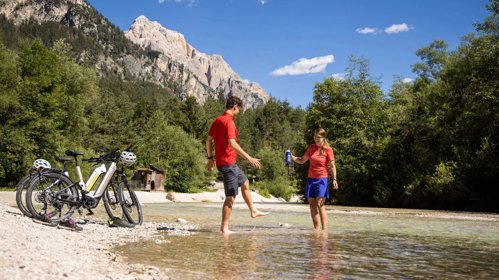Two cyclists taking a water break at a mountain river shore