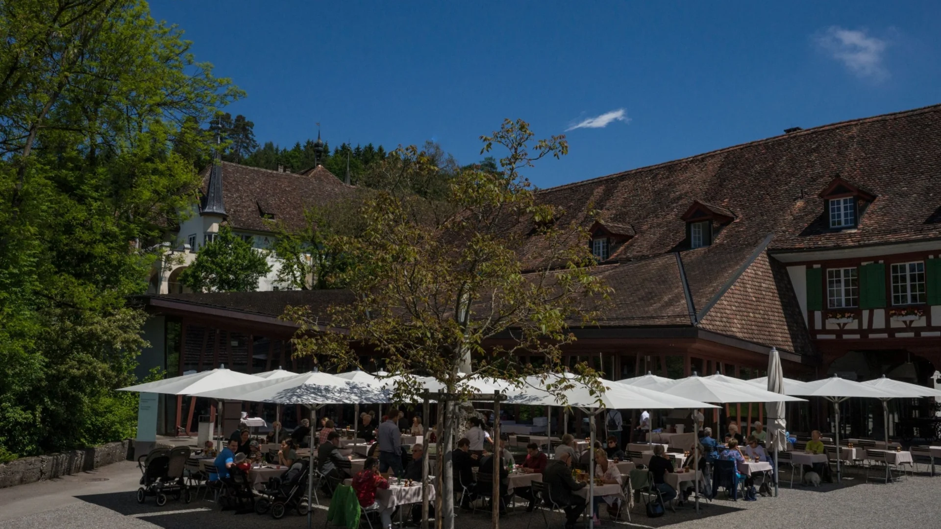 Mensen eten buiten bij een restaurant onder witte parasols