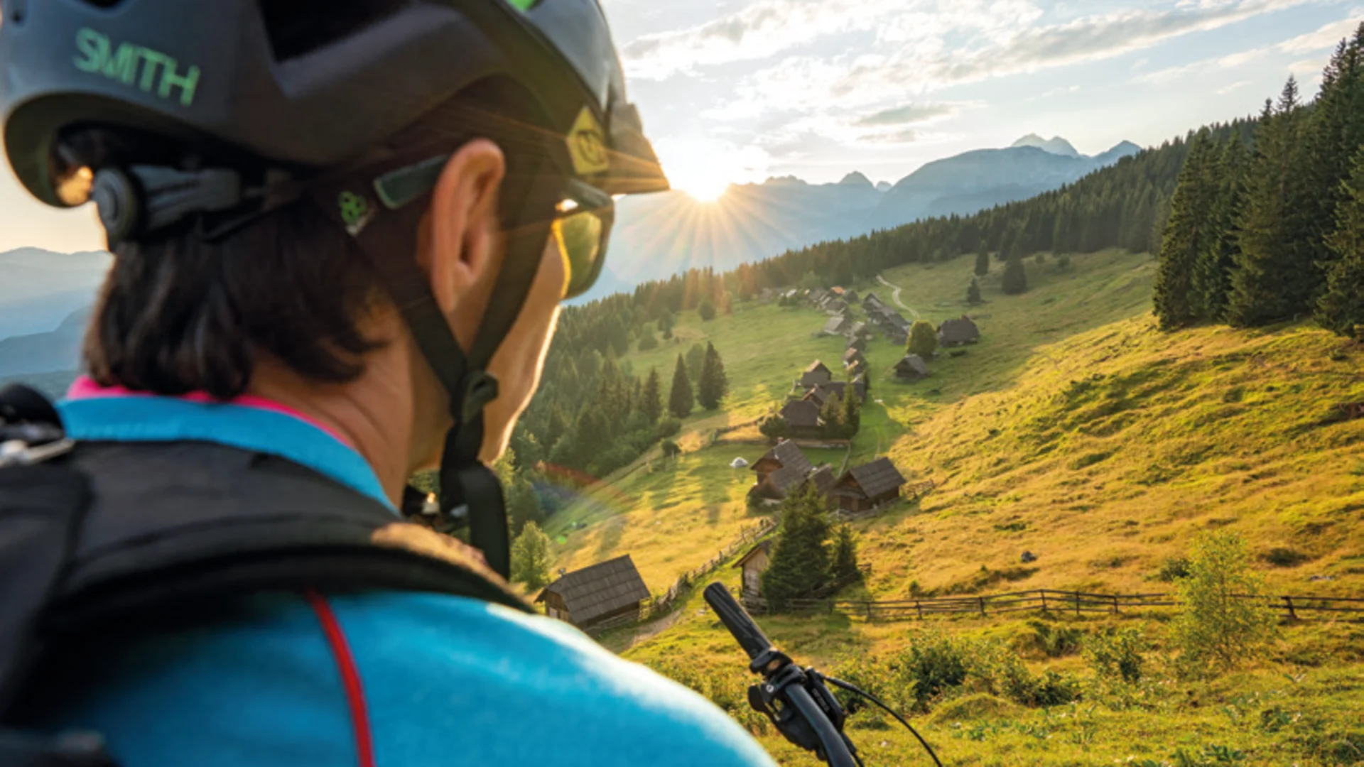 Mountainbiker kijkt uit over dal met huizen en zonsondergang in de bergen