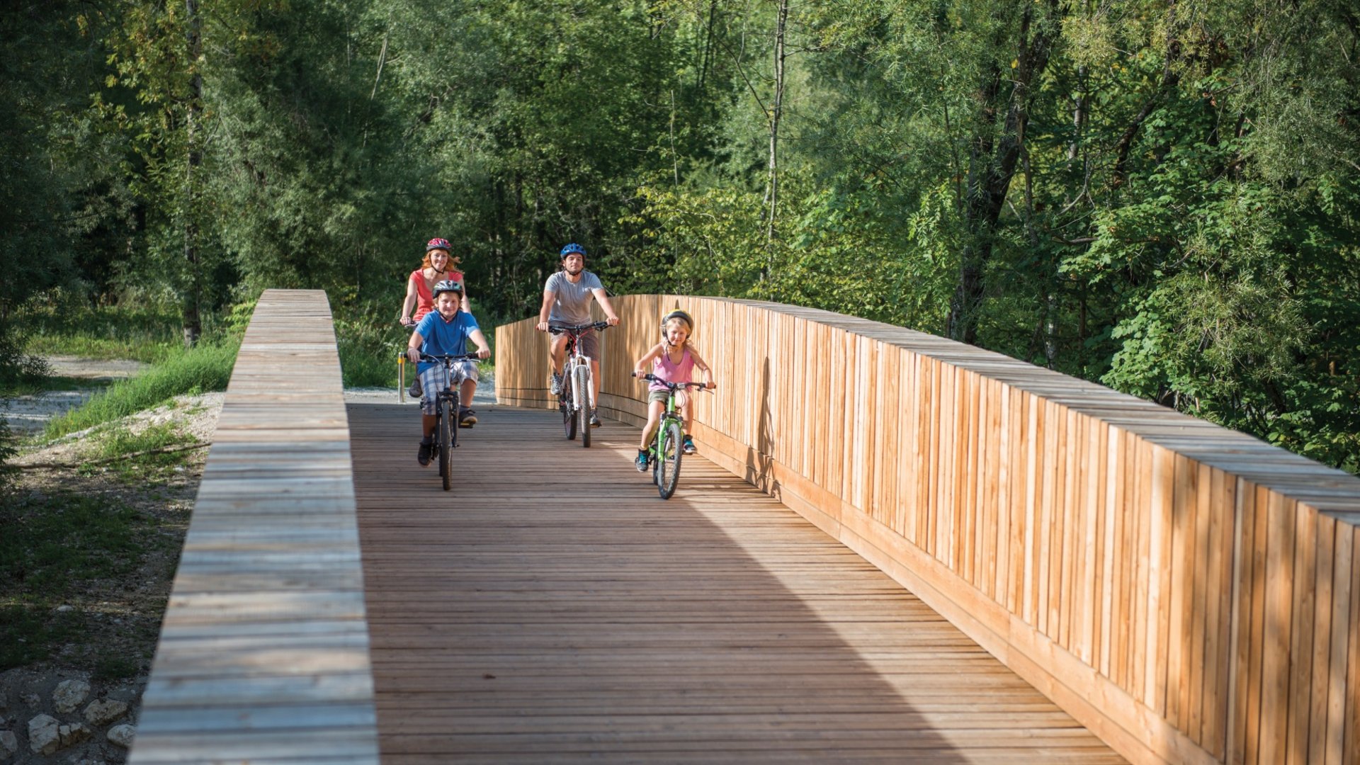 Family of four cycling on a wooden bridge surrounded by trees