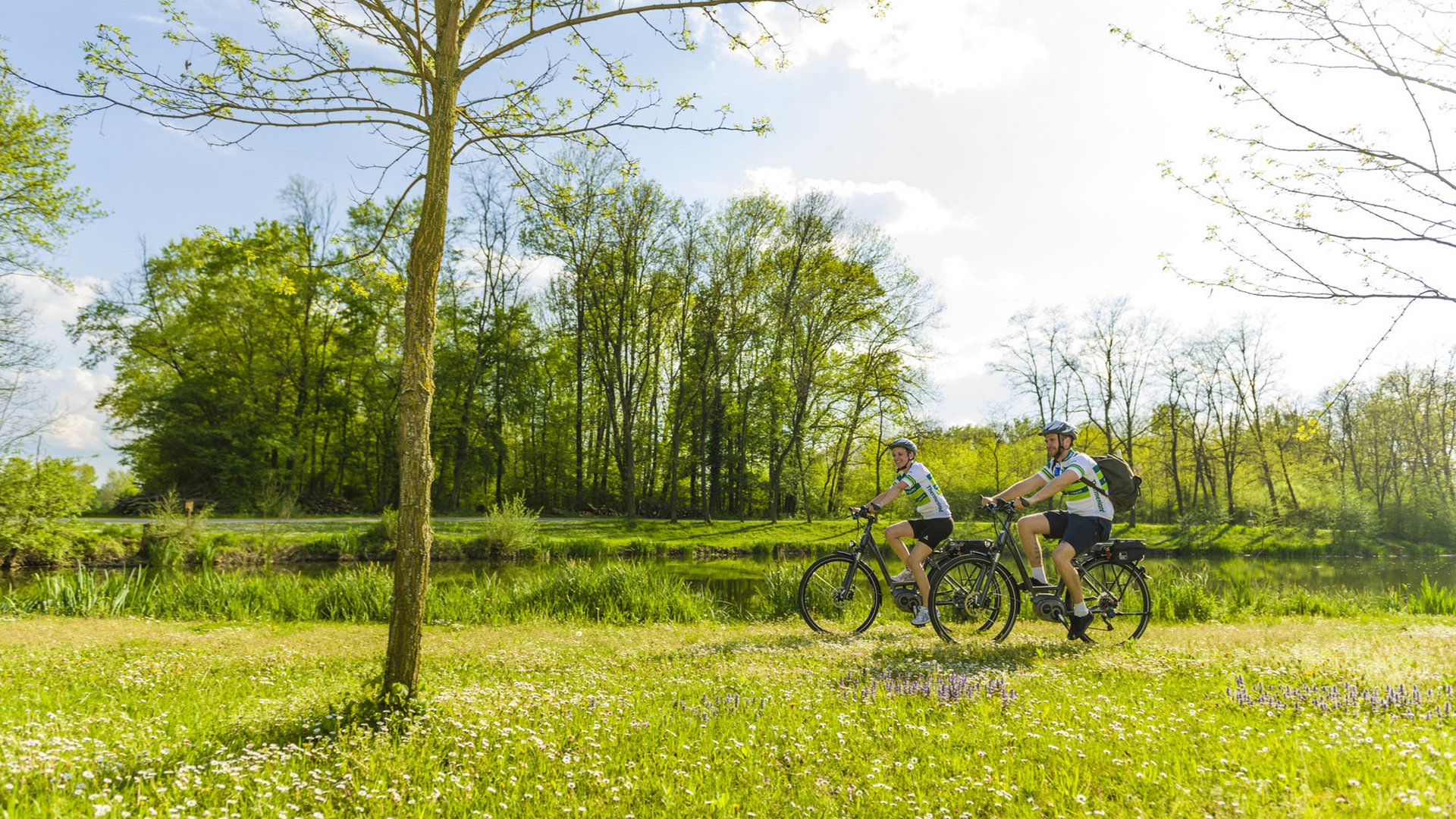 Zwei Radfahrer fahren entlang eines Flusses in der grünen Frühlingslandschaft