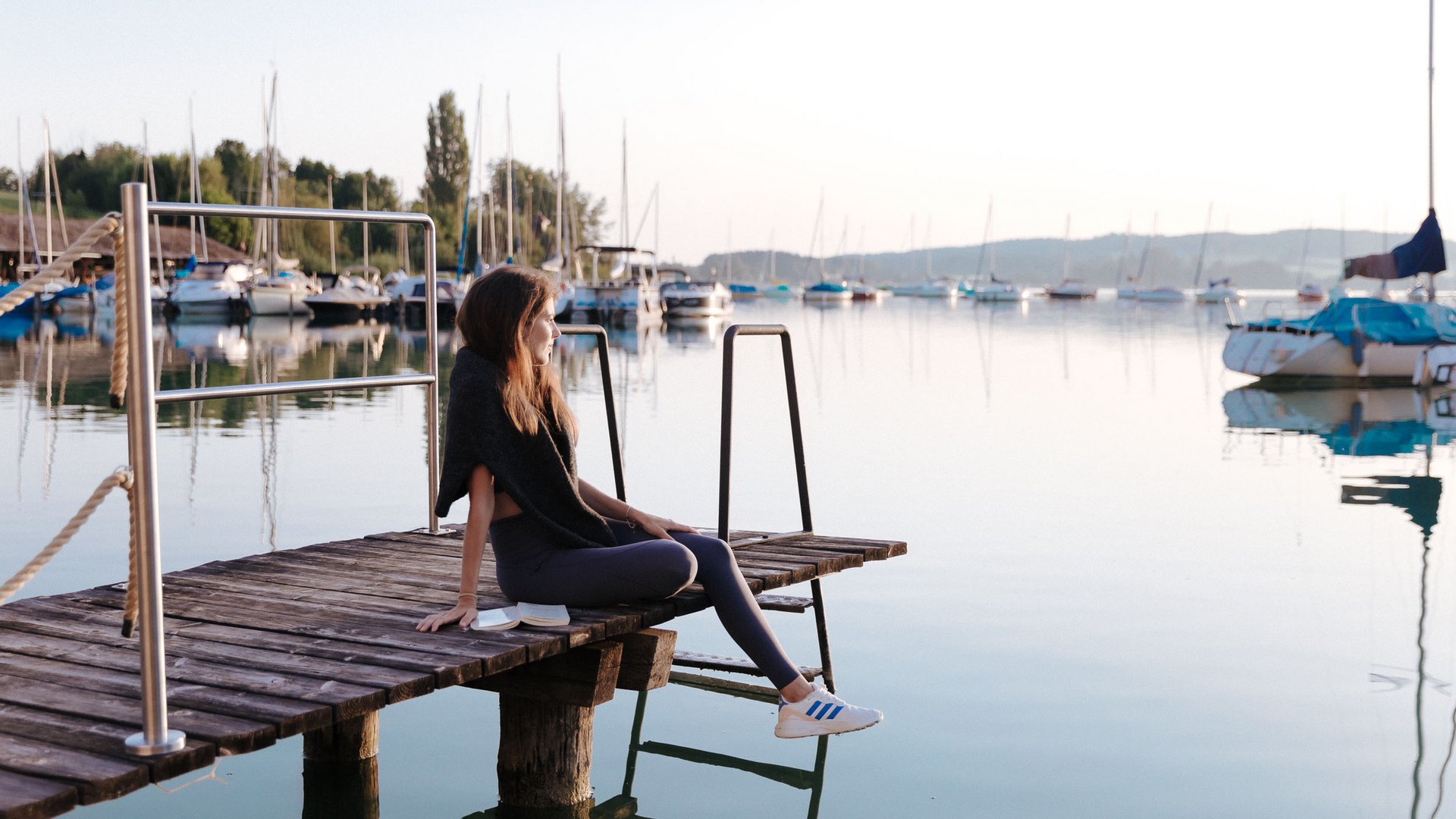 Woman sitting on dock looking at calm harbor with sailboats