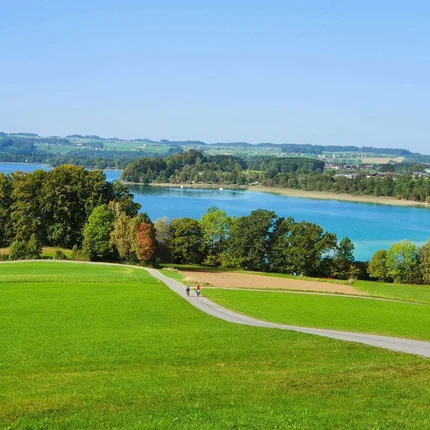 Groene weilanden, paden en een blauw meer onder een heldere lucht