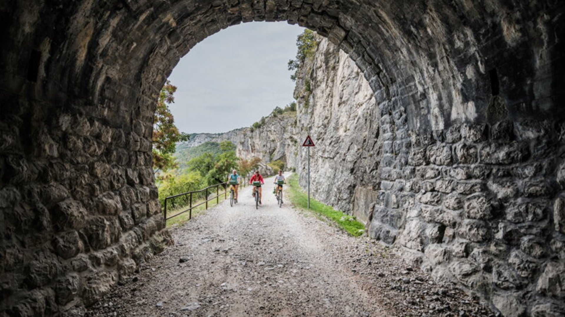 Three cyclists riding through a tunnel on a mountain trail