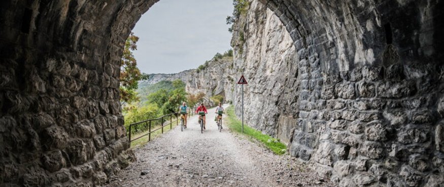 Three cyclists riding through a tunnel on a mountain trail