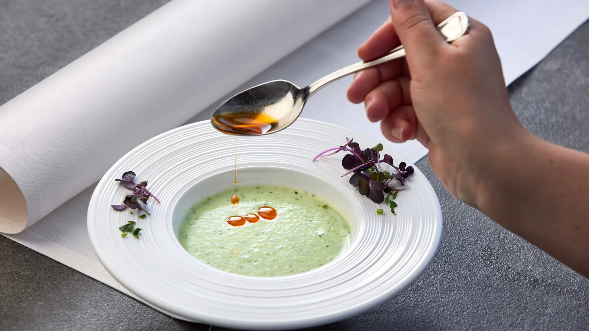 Garden & Spa Hotel das Götzfried **** © Michael Huber Fotographie Hand druppelt olie in groene soep op wit bord met kruiden