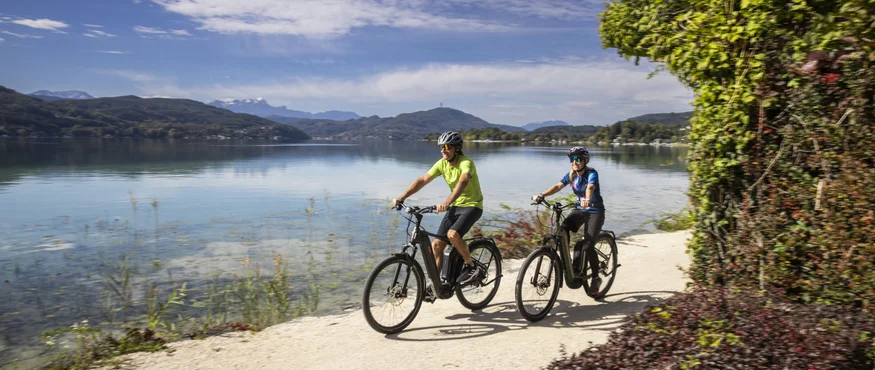 Zwei Radfahrer fahren auf einem Weg am See entlang bei sonnigem Wetter