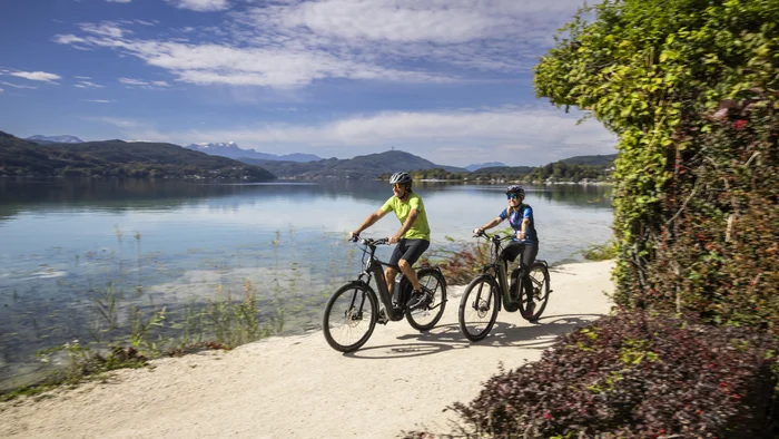 Klagenfurt kann mehr als Wörthersee! © Velontour - Heiko Mandl Zwei Radfahrer fahren auf einem Weg am See entlang bei sonnigem Wetter