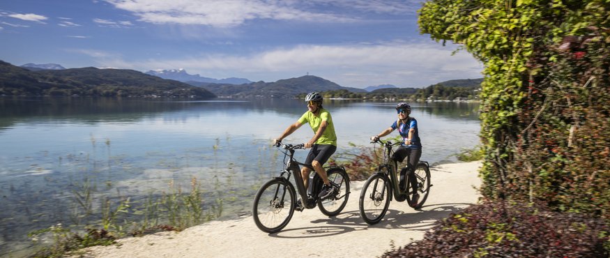Two cyclists biking on a lakeside path on a sunny day