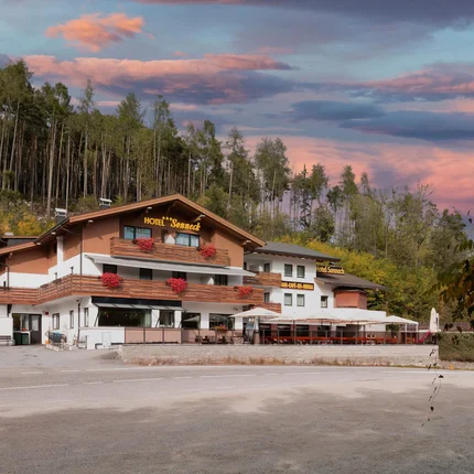 Hotel mit Terrasse vor Wald und buntem Abendhimmel