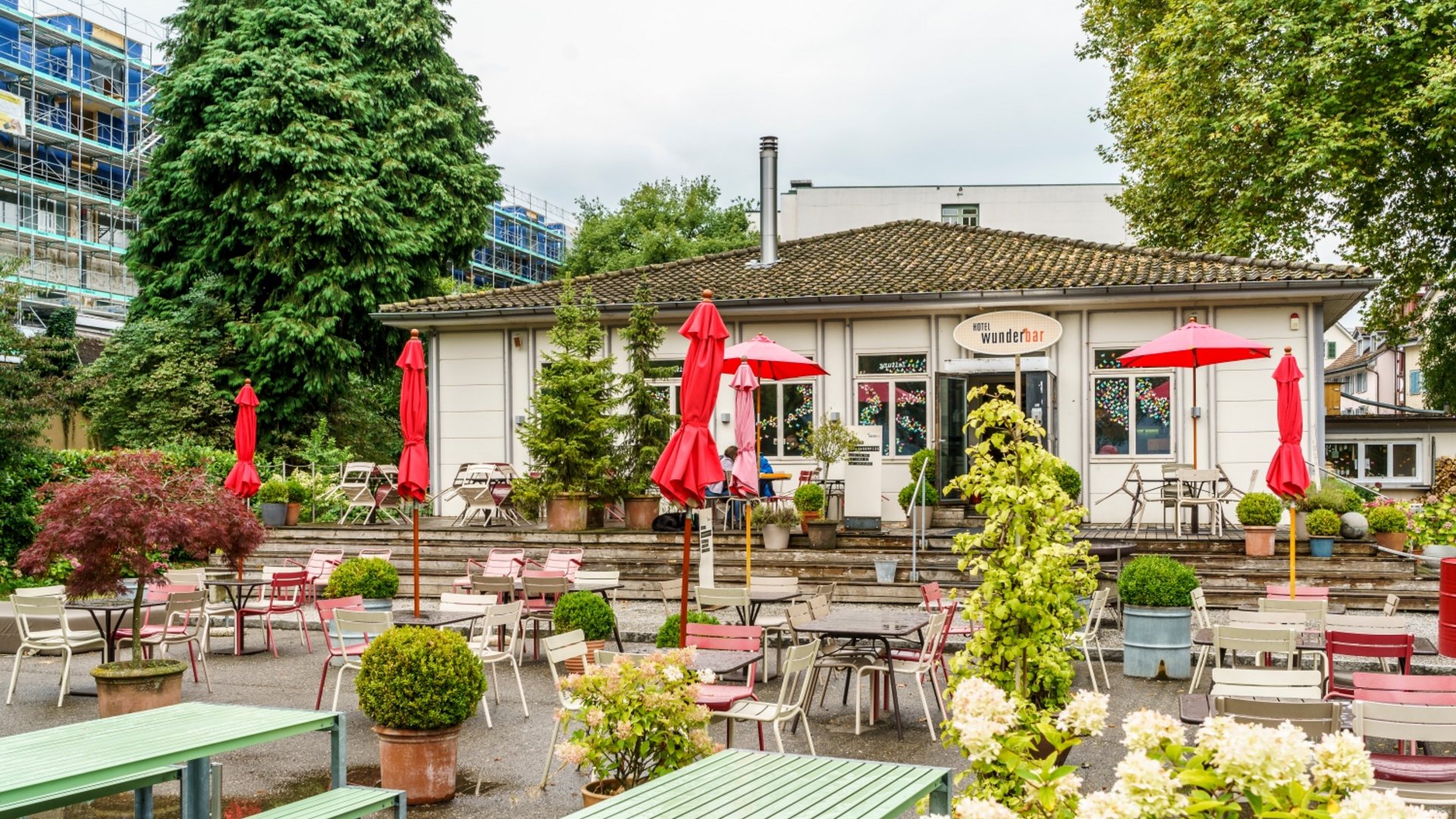 Empty outdoor seating area of a café with red umbrellas and plants