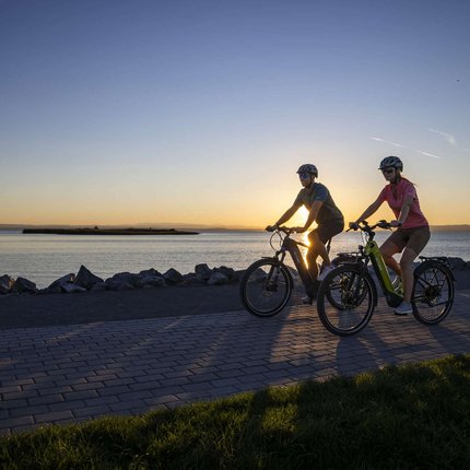 Zwei Radfahrer fahren bei Sonnenuntergang am Wasser entlang