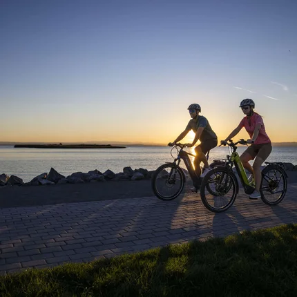 Zwei Radfahrer fahren bei Sonnenuntergang am Wasser entlang