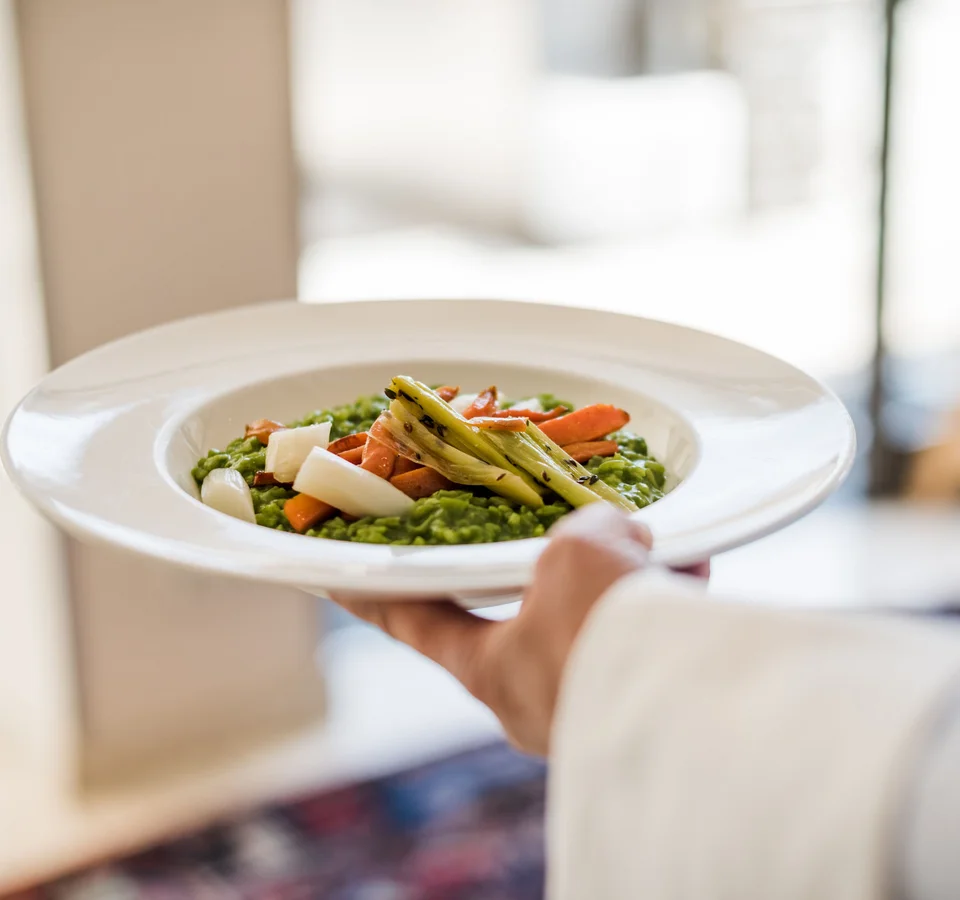 Bediener draagt bord met groene risotto en gegrilde groenten