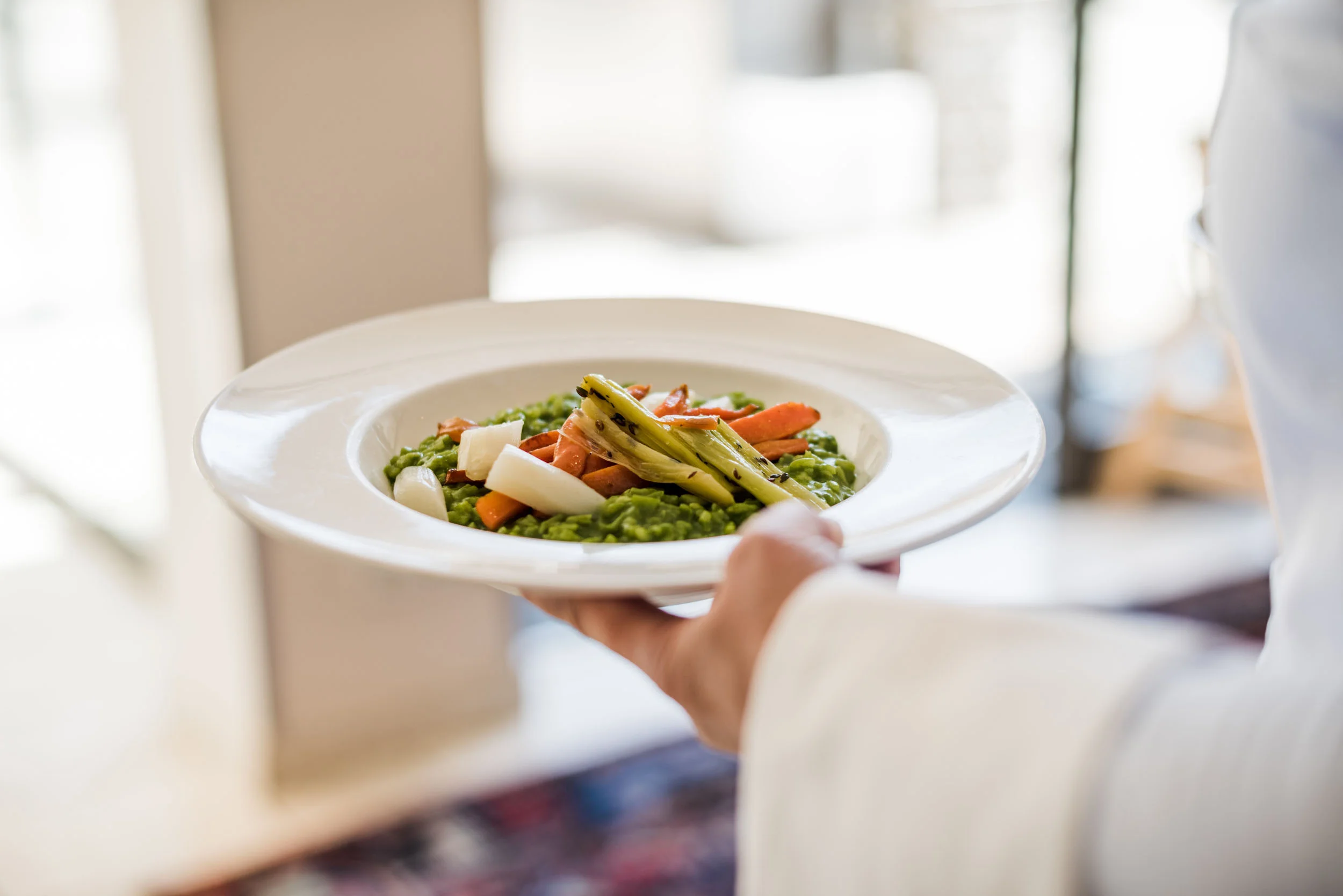 Bediener draagt bord met groene risotto en gegrilde groenten
