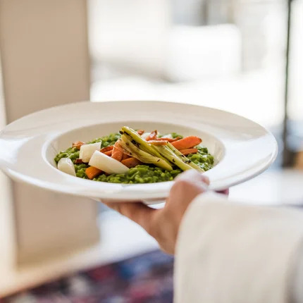 Bediener draagt bord met groene risotto en gegrilde groenten