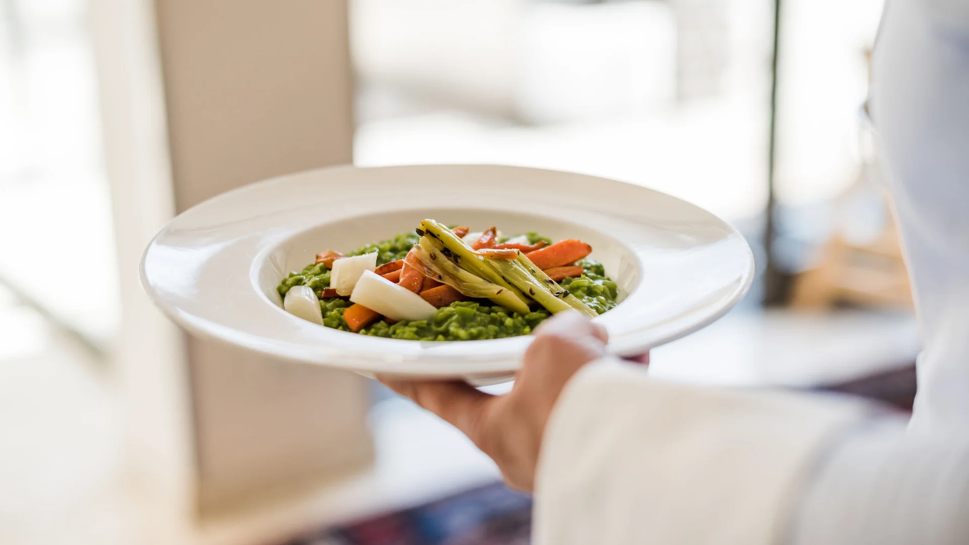Anthering: Radurlaub zwischen Moor & Mozartstadt © Hotel Ammerhauser Servierender hält Teller mit grünem Risotto und Gemüse