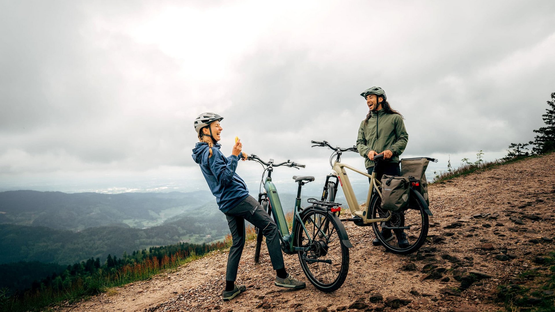 Victoria Two cyclists with helmets on a mountain trail under cloudy sky