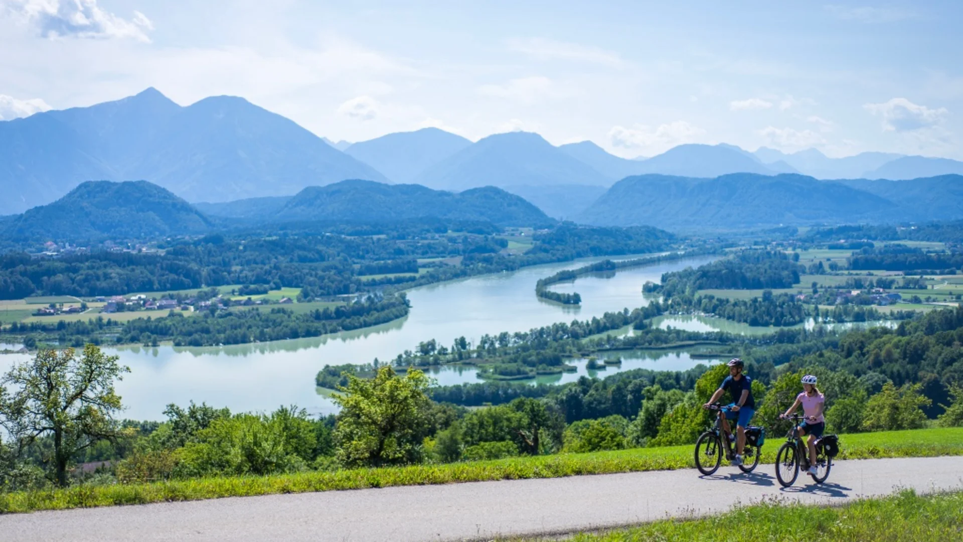 Twee fietsers op bergweg met rivier en bergen op de achtergrond