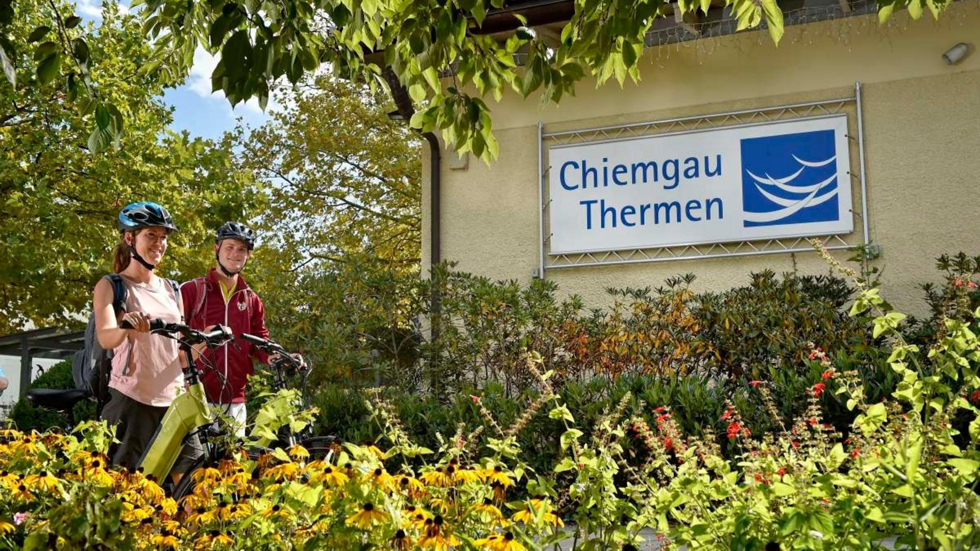 Two cyclists at the entrance of Chiemgau Thermen in a flower garden