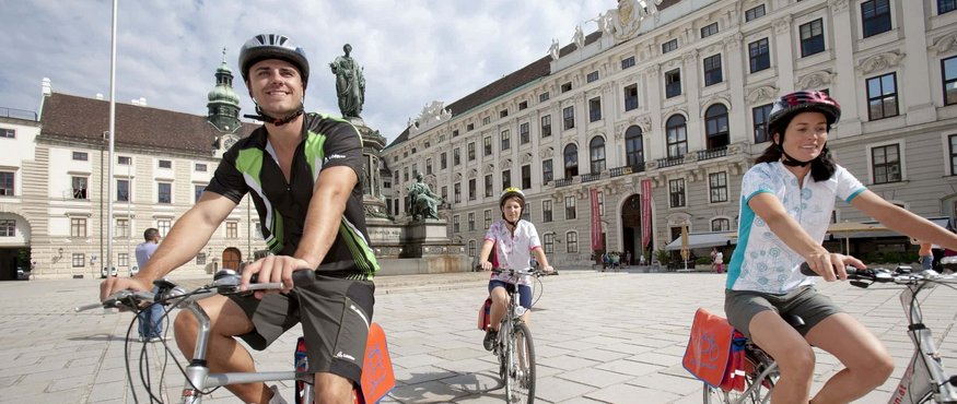 Three cyclists riding bikes near a historic building in the city