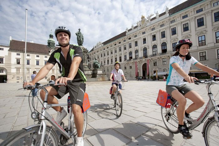 Three cyclists riding bikes near a historic building in the city