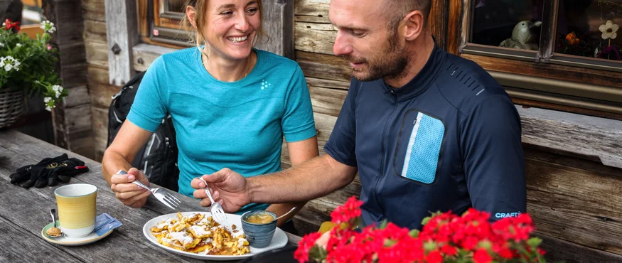Paar isst Kuchen und trinkt Kaffee auf Holztisch vor Holzhütte